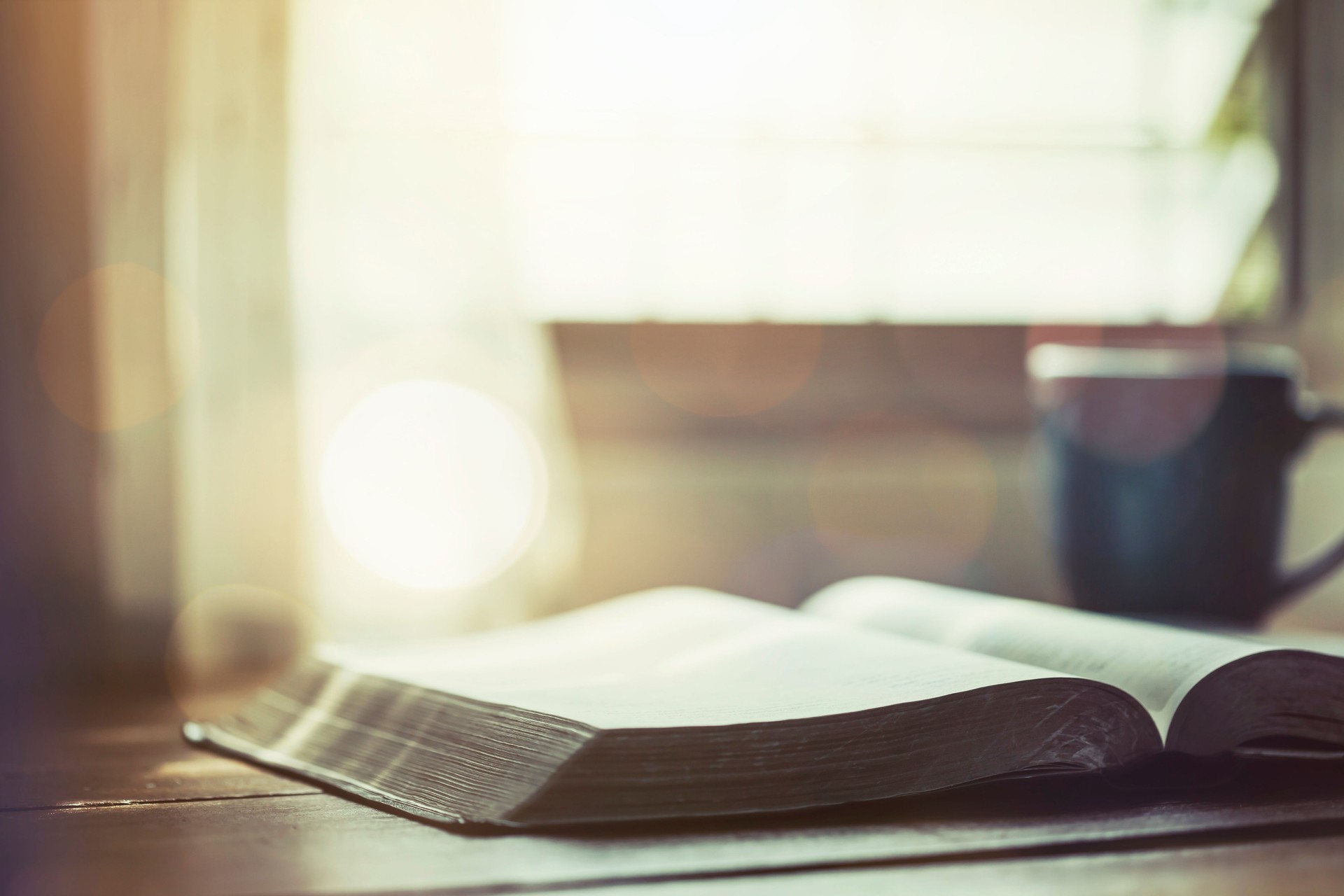 open bible with a coffee cup on wooden table near window, morning devotion concept